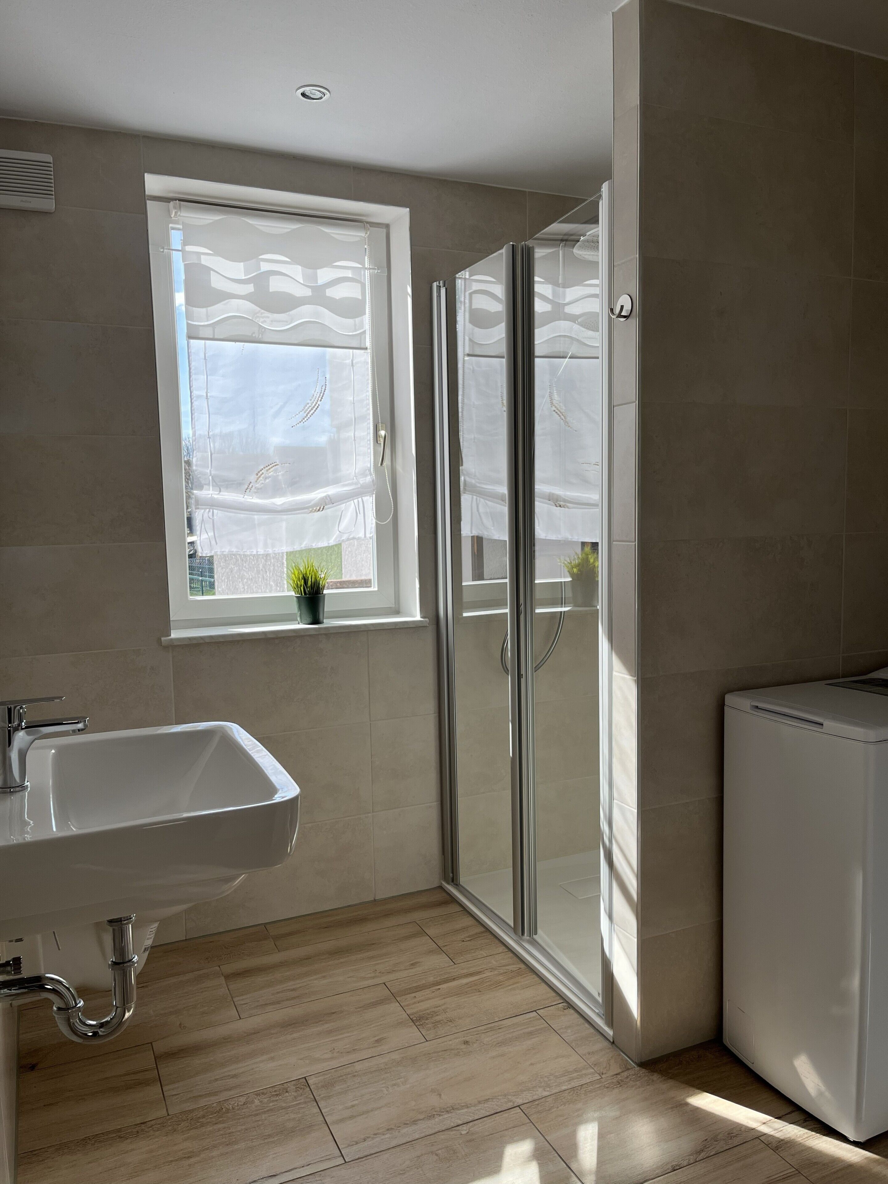 A modern bathroom with a sink, a glass shower enclosure, and a window with a view.