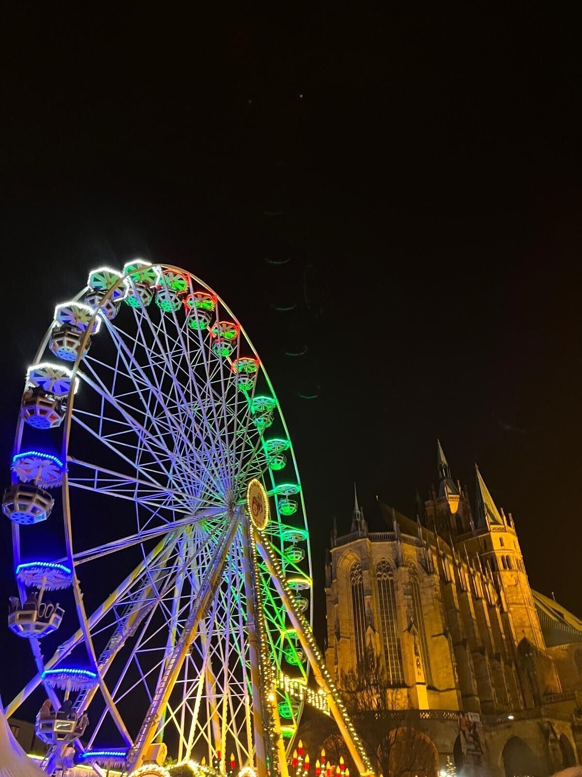 Una noria grande con luces de colores y un edificio histórico al fondo.