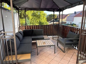 Un área de estar al aire libre techada, con un sofá, sillas y una mesa.