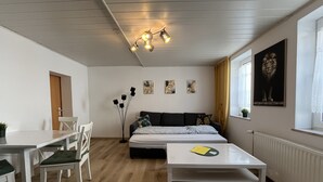 A modern living room with a sofa, a dining table with chairs, a coffee table, and a floor lamp. - Apartment '2 Ferienwohnung Junghanß' with Wi-Fi (Blankenhain)