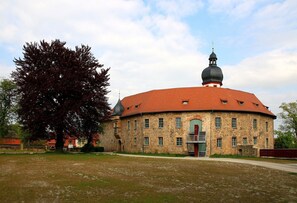 A stone building with a red roof and a central dome, surrounded by a grassy area and trees. - Apartment '2 Ferienwohnung Junghanß' with Wi-Fi (Blankenhain)