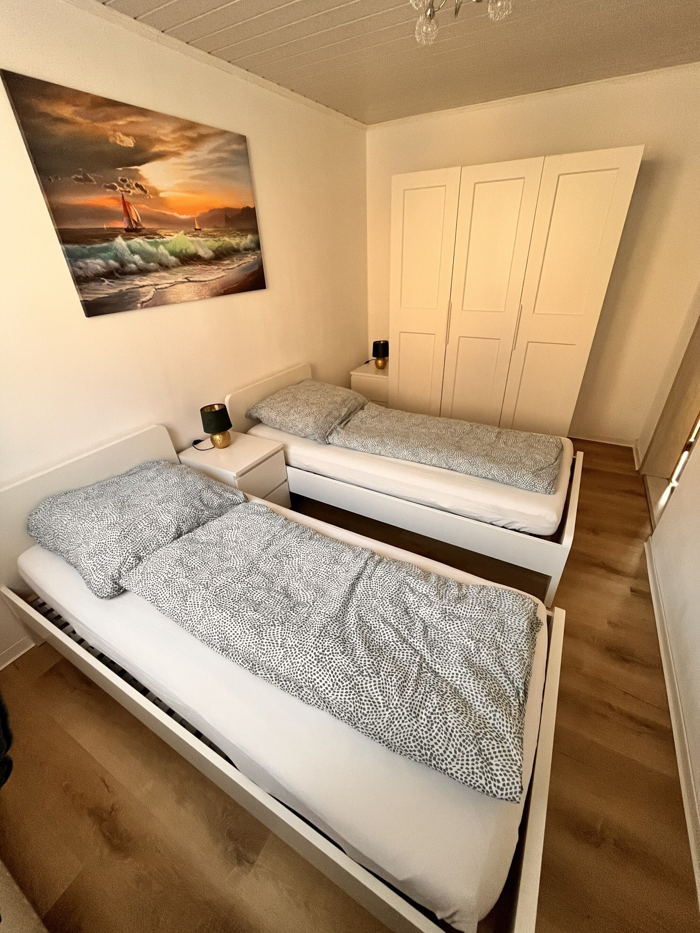 Ett sovrum med två enkelsängar, ett nattduksbord med en lampa, en tavla på väggen och en garderob.