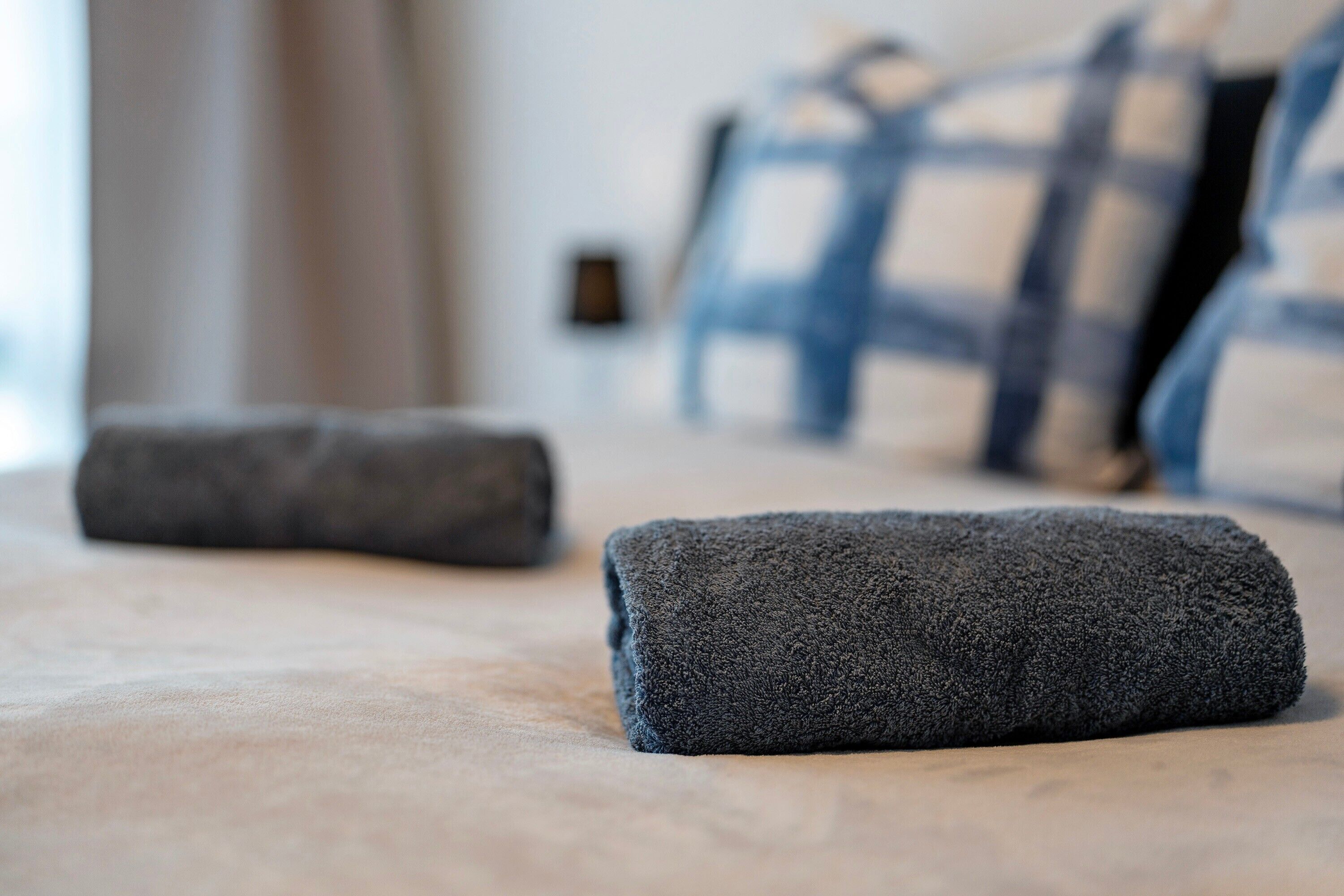 A neatly made bed with a dark grey blanket and a pillow in a hotel room.