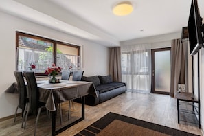 A modern living room with a sofa, dining table, chairs, and a TV.