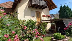 Une maison avec un balcon, un toit en bois et un jardin où poussent des fleurs roses.