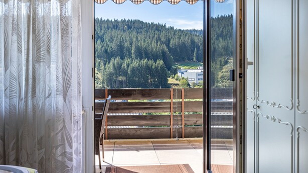 Een kamer met een schuifdeur naar een balkon met uitzicht op een bebost helling.