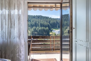 Quarto com porta de vidro deslizante que dá para uma varanda com vista para uma encosta arborizada.