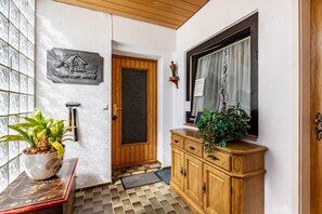 A wooden door with a glass panel, a potted plant on a table, a cabinet with drawers, and a wall-mounted plaque.