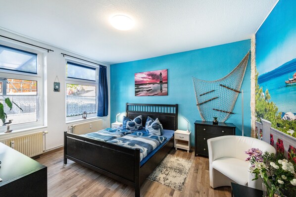 Een slaapkamer met een bed, nachtkastjes, een stoel, een raam en een muurschildering.