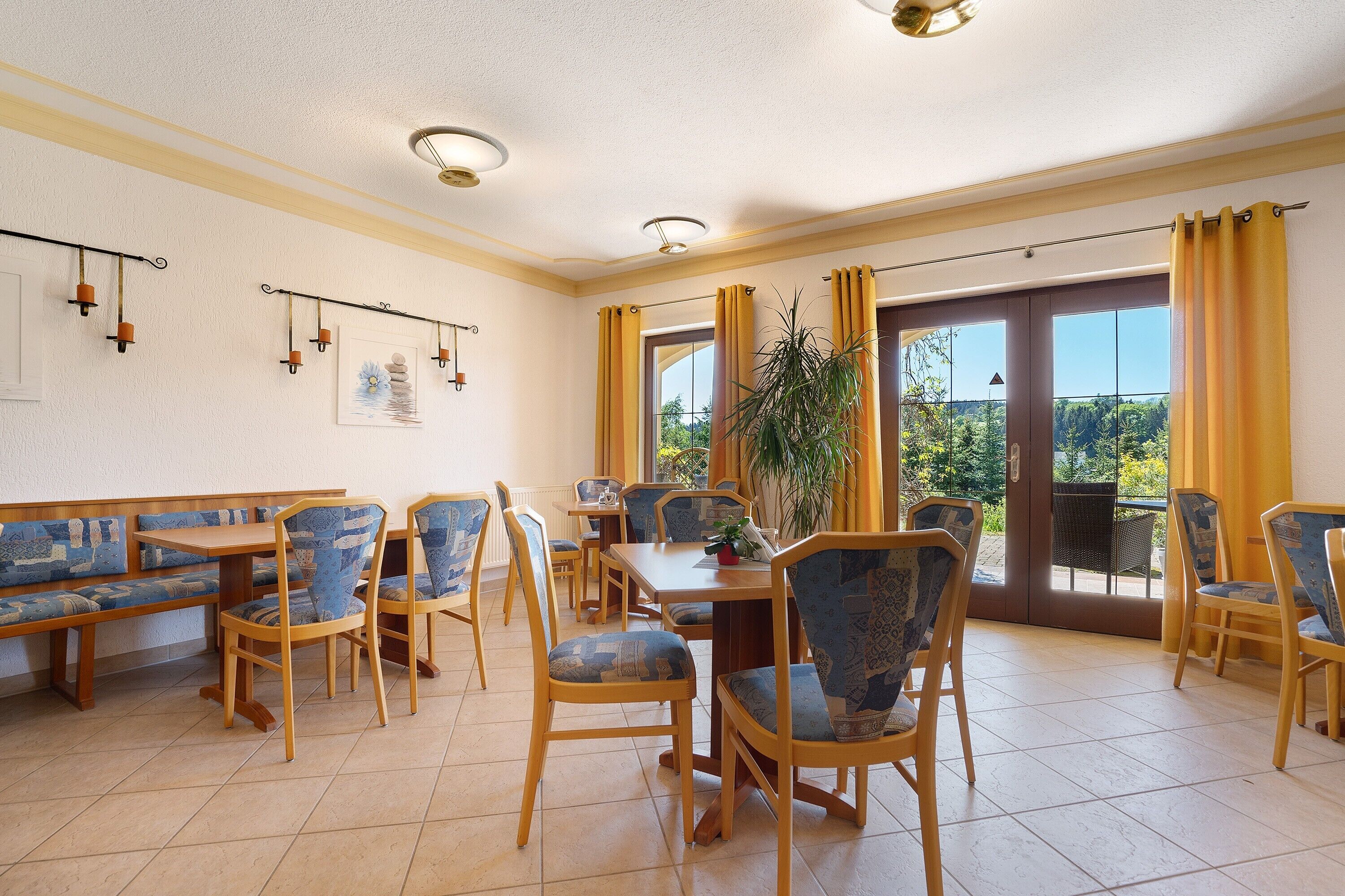 A dining area with wooden tables and chairs, a bench, and a large window with curtains.