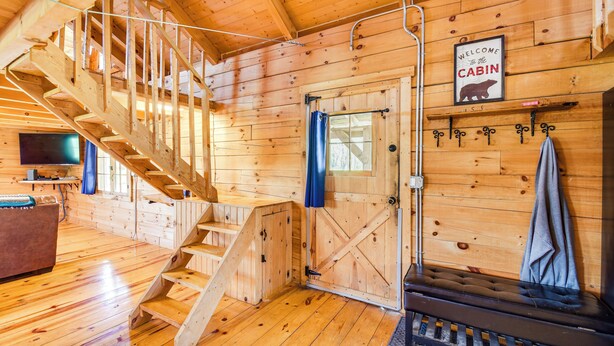 A cabin interior with wooden walls, a staircase, a bench, and a welcome sign. - Bellevue Log Cabin w/ Gas Grill & Creek Access (Bellevue)