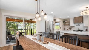 Une cuisine moderne dotée d’un grand îlot central, d’une table à manger en bois et de luminaires suspendus.