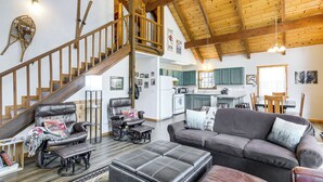 Ein großzügiger Wohnbereich mit hoher Decke, einer Holztreppe und einer gemütlichen Sitzecke mit Sofa und Relaxliegen.