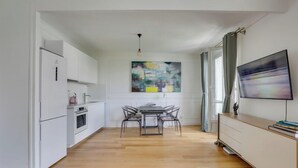 A modern kitchen with white cabinetry, a dining area with a table and chairs, and a large abstract painting above the table. - 705 Suite Lecourbette - Superb apartment (Paris 15 Vaugirard)