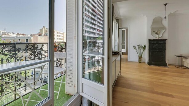A spacious room with a large window, a balcony with a metal railing, a fireplace, and a wooden floor. - 705 Suite Lecourbette - Superb apartment (Paris 15 Vaugirard)