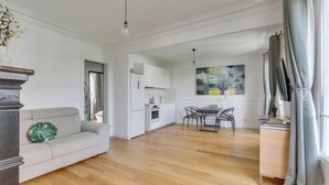 A spacious living area with a sofa, a dining table with chairs, a kitchen in the background, and a large window with curtains. - 705 Suite Lecourbette - Superb apartment (Paris 15 Vaugirard)