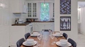 Eine moderne Küche mit weißen Schränken, einem Holzespeisetisch, der für sechs Personen gedeckt ist, und zwei gerahmten abstrakten Bildern an der Wand.