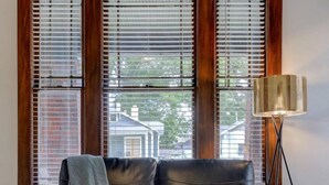 Ein schwarzes Ledersofa mit grauer Decke, eine Stehlampe und Blick durch große Fenster mit Jalousien.