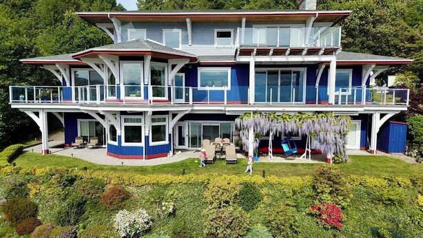A two-story house with a balcony, surrounded by a garden with various plants and flowers. - Blue House (Gibsons)