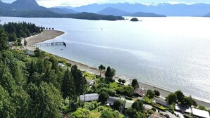 A coastal area with a pier extending into the water, surrounded by lush greenery and residential buildings. - Blue House (Gibsons)