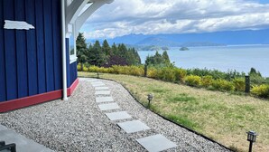 A house with a blue exterior, a gravel pathway leading to a porch, and a view of a lake and mountains in the background. - Blue House (Gibsons)