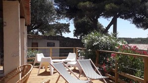 A wooden deck with lounge chairs and a wicker chair, overlooking a garden with trees and flowers. - Maison Proche du Port, vue sur la Citadelle (Bonifacio)