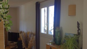 A room with a wooden floor, a television, a wooden cabinet, and a window with curtains. - Maison Proche du Port, vue sur la Citadelle (Bonifacio)