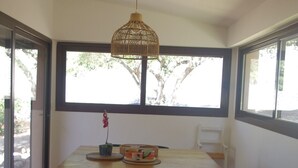 A dining area with a wooden table, two black chairs, a woven pendant light, and a view through large windows. - Maison Proche du Port, vue sur la Citadelle (Bonifacio)