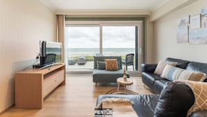 Ein modernes Wohnzimmer mit Fernseher, Sofa und Meerblick.