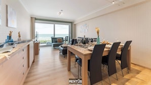 Ein moderner Essbereich mit Holztisch und -stühlen, einer Küchenarbeitsplatte mit Schränken und einem großen Fenster mit Blick ins Freie.