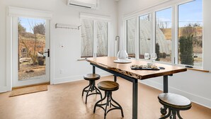 Une pièce spacieuse avec une grande table, deux tabourets et une vue sur l’extérieur grâce à de grandes fenêtres.
