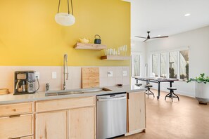 A modern kitchen with wooden cabinets, a dishwasher, a coffee maker, and a ceiling fan.