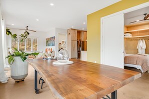 A modern kitchen with a wooden countertop, a dining area with a table and chairs, and a view of a bedroom with a bed and a closet.
