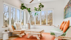 Un salon moderne avec de grandes fenêtres, un canapé en bois, une petite table et un divan vert.