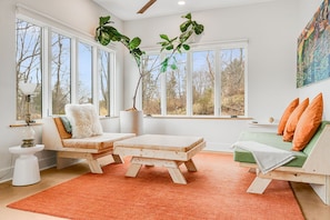 A modern living room with large windows, a wooden sofa, a small table, and a green couch.
