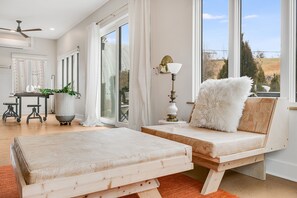 A modern living room with a large window, a sofa, a lamp, and a dining area with a table and chairs.