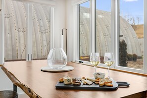 A table with a cheese board, two glasses of white wine, and a clear glass vase.