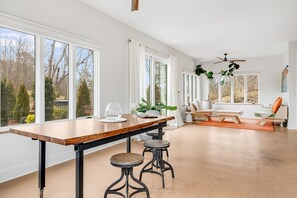 A spacious room with a large dining table, two stools, a sofa, and a ceiling fan.