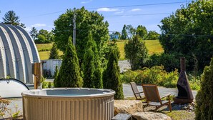 Un bain à remous avec deux fauteuils, entouré de rochers et de verdure, avec une serre et une maison en arrière-plan.