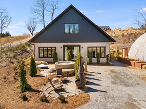 A modern two-story house with a patio, outdoor seating, and a hot tub.