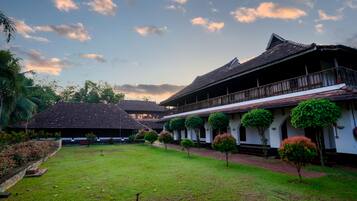 A traditional building with a balcony, surrounded by a well-maintained lawn and small trees.