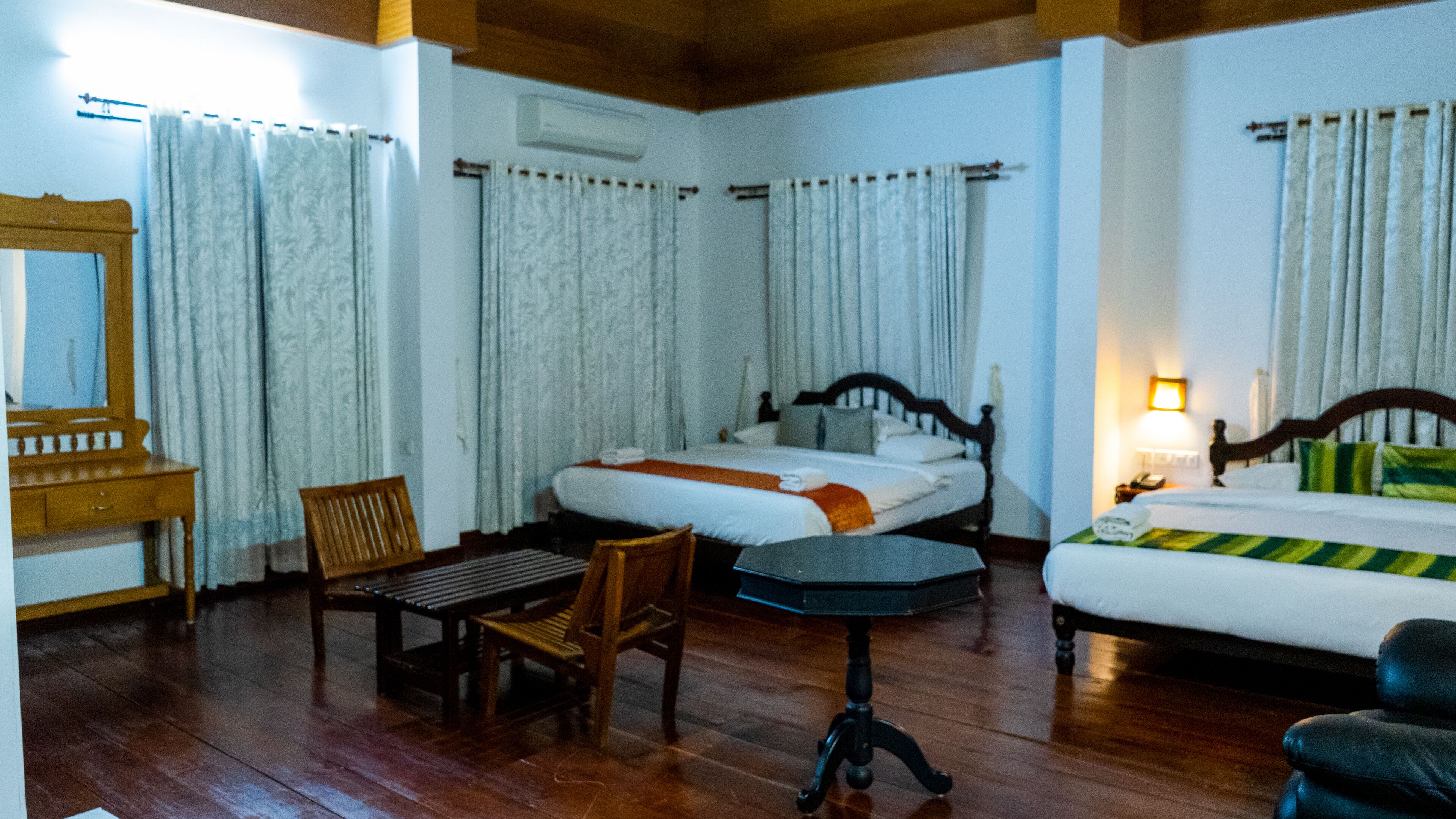 A hotel room with two beds, a wooden chair, a small table, and a mirror.