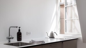 Una cocina moderna con un lavamanos de acero inoxidable, una botella de jabón para manos y una tetera sobre la encimera.