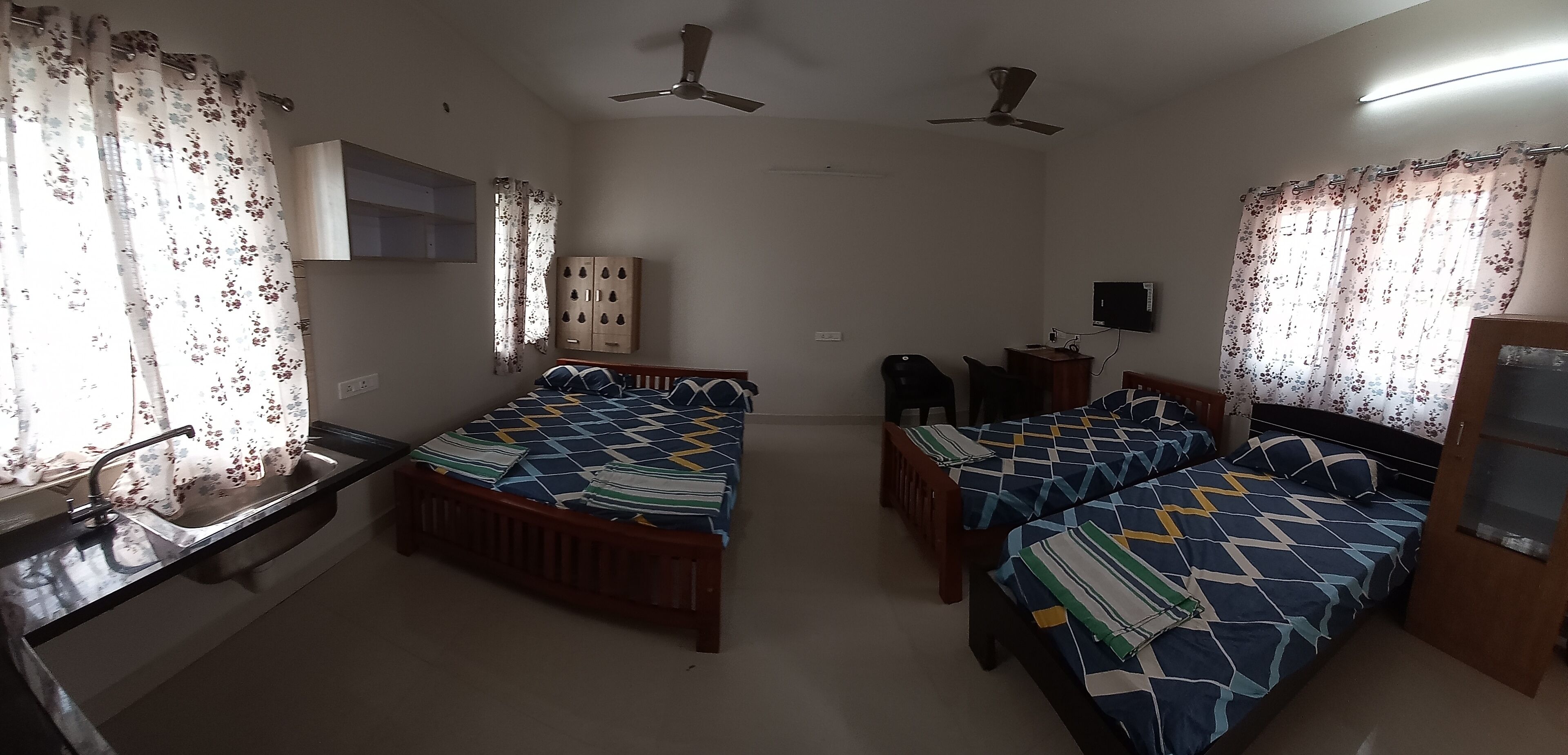 A bedroom with two single beds, a desk with a chair, a wardrobe, and a television.