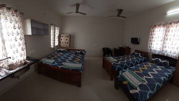 A bedroom with two single beds, a desk with a chair, a wardrobe, and a television.