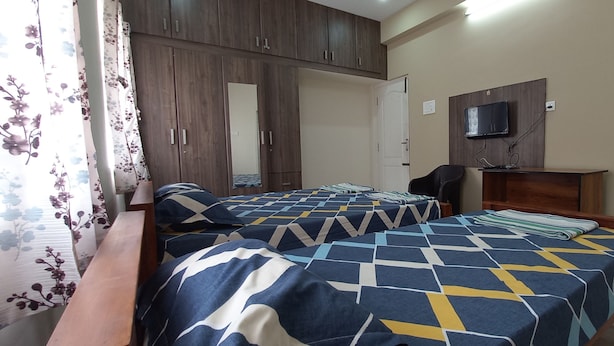 Een slaapkamer met twee bedden, een houten kledingkast en een televisie aan de muur.