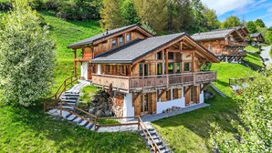 A chalet-style building with a balcony, surrounded by lush greenery and a mountain backdrop. - Gingembre 12 by Interhome (Nendaz)