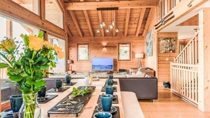 A spacious wooden interior with a long dining table, comfortable seating, and a television in the background. - Gingembre 12 by Interhome (Nendaz)