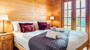 A wooden cabin room with a bed, two bedside tables with lamps, and a large window with a view of the outdoors. - Gingembre 12 by Interhome (Nendaz)