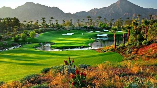 Campo de golf con montañas al fondo, elementos acuáticos y palmeras.